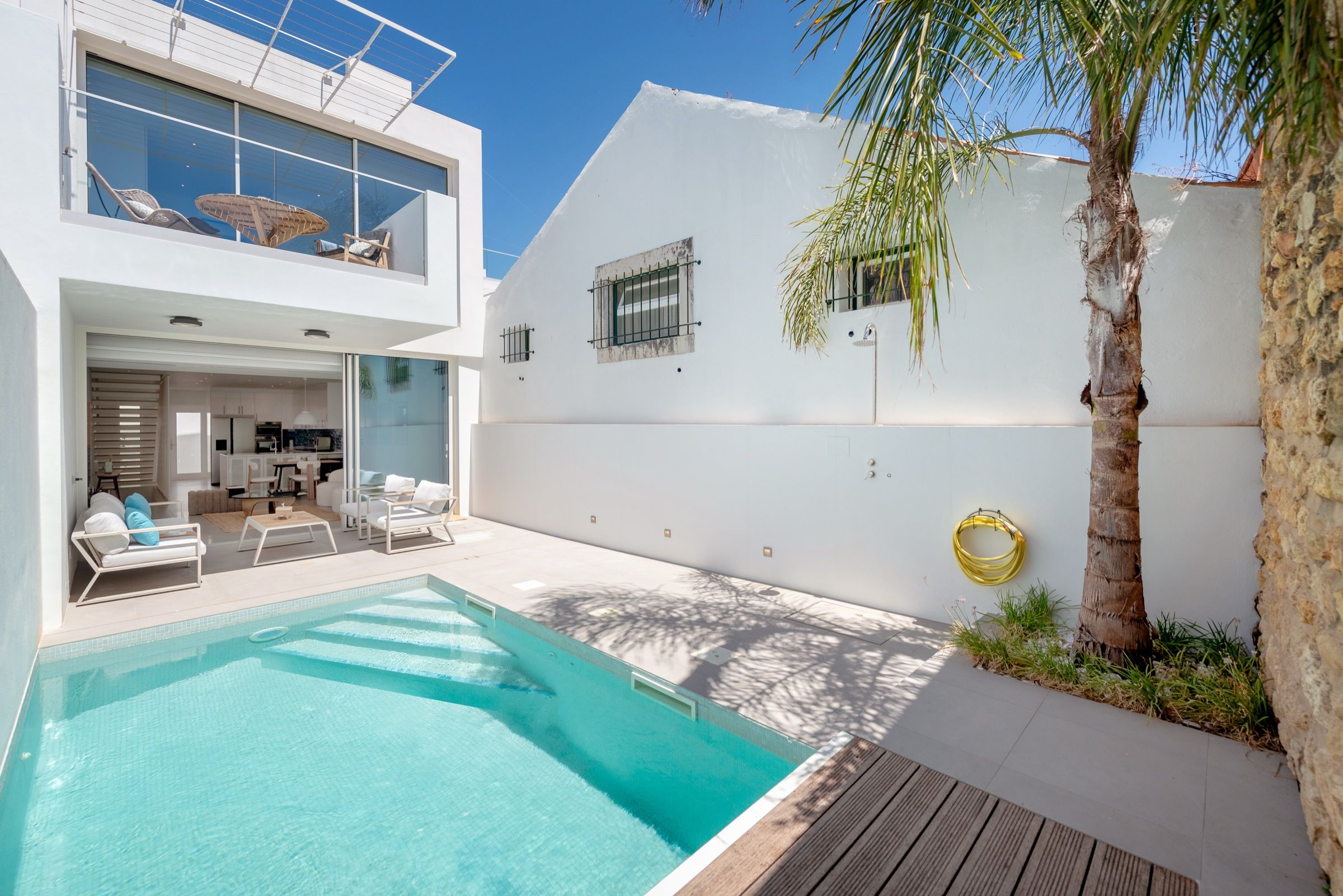 Courtyard of a white house in the old town of Lagos, with a pool, a palm tree and the glazed living room opening onto it