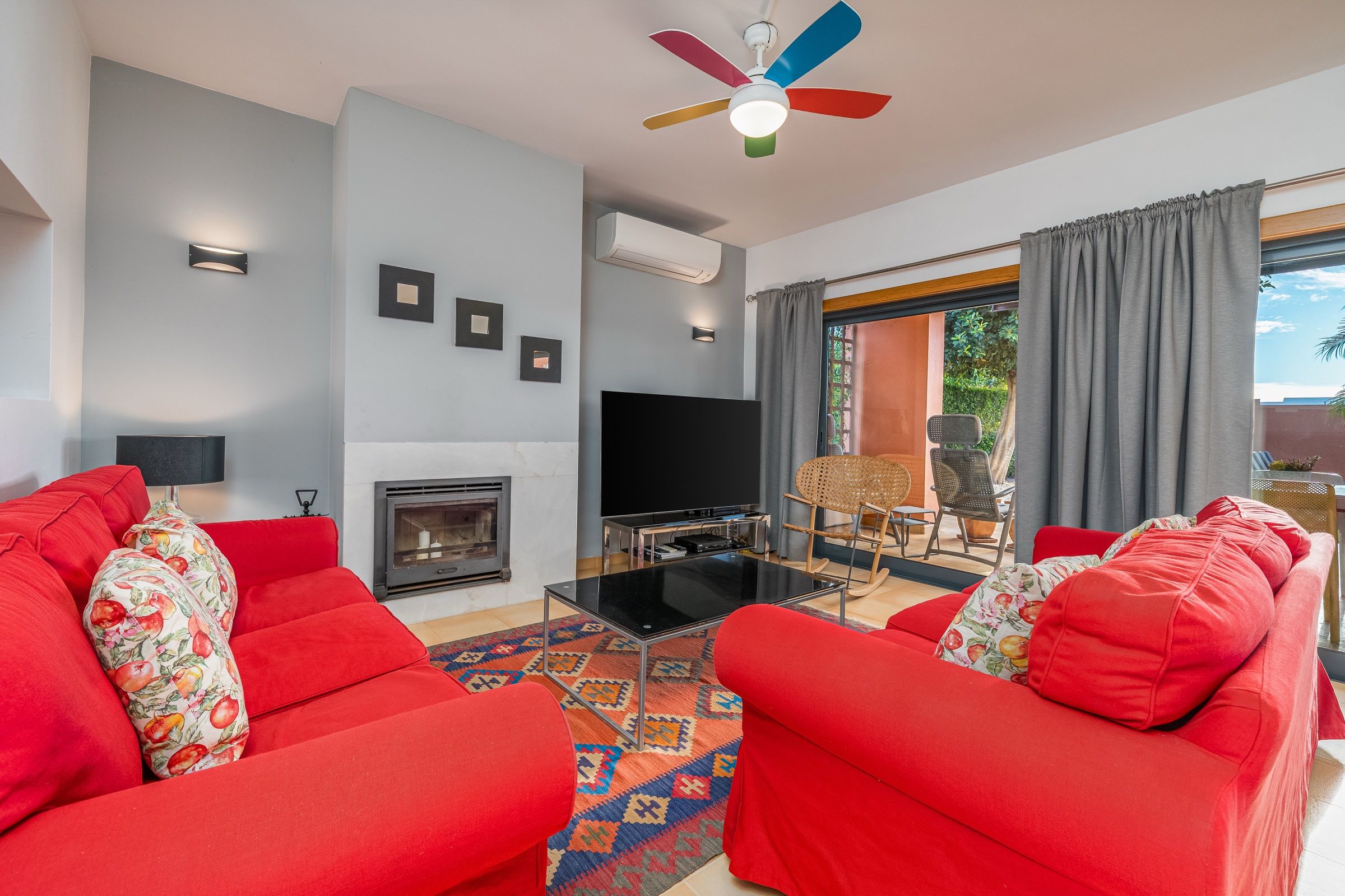 Living room with two red sofas, a fireplace, a patterned rug and a glass door to the garden