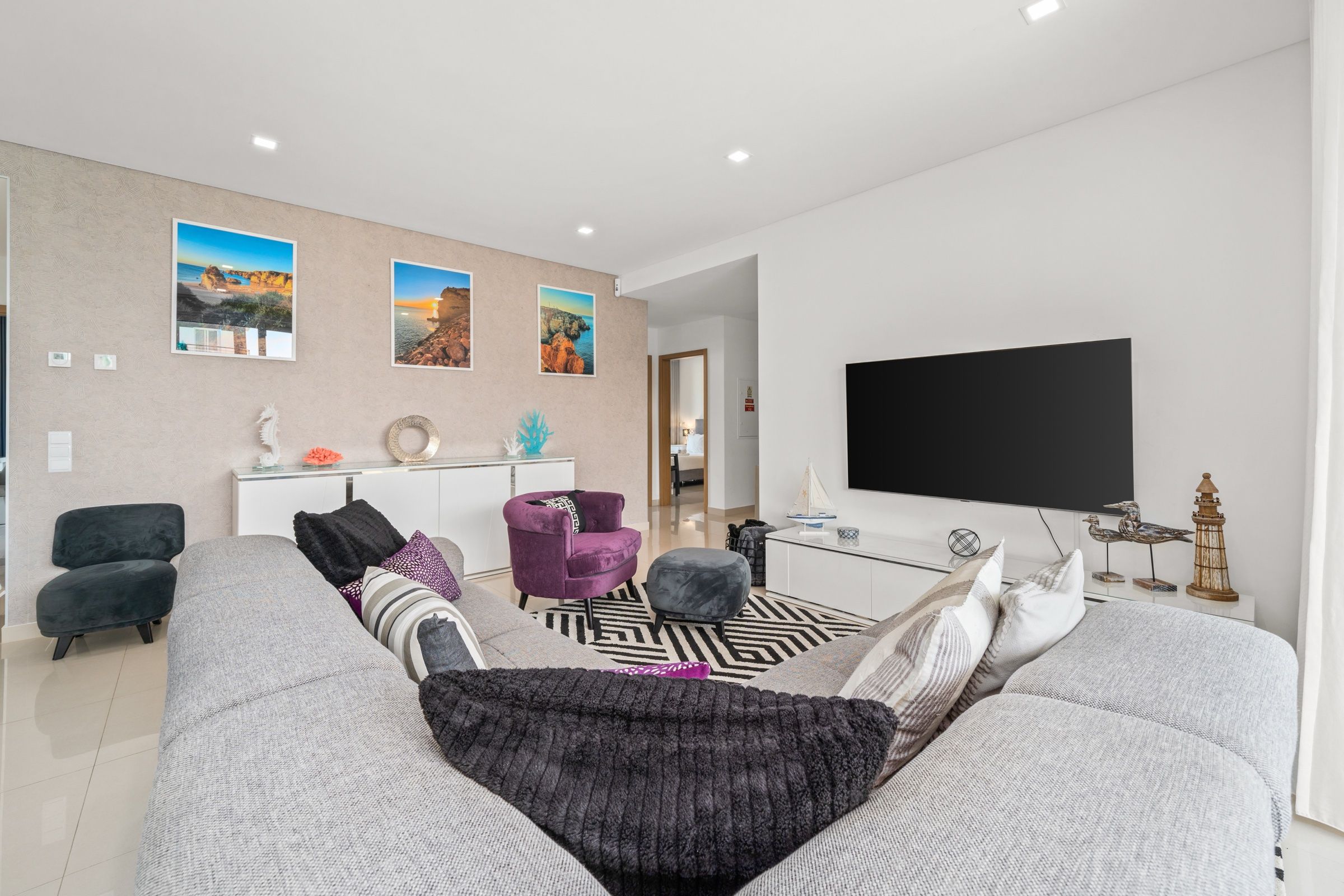 Living room with a grey corner sofa, armchairs, a black and white rug and a wall-mounted TV
