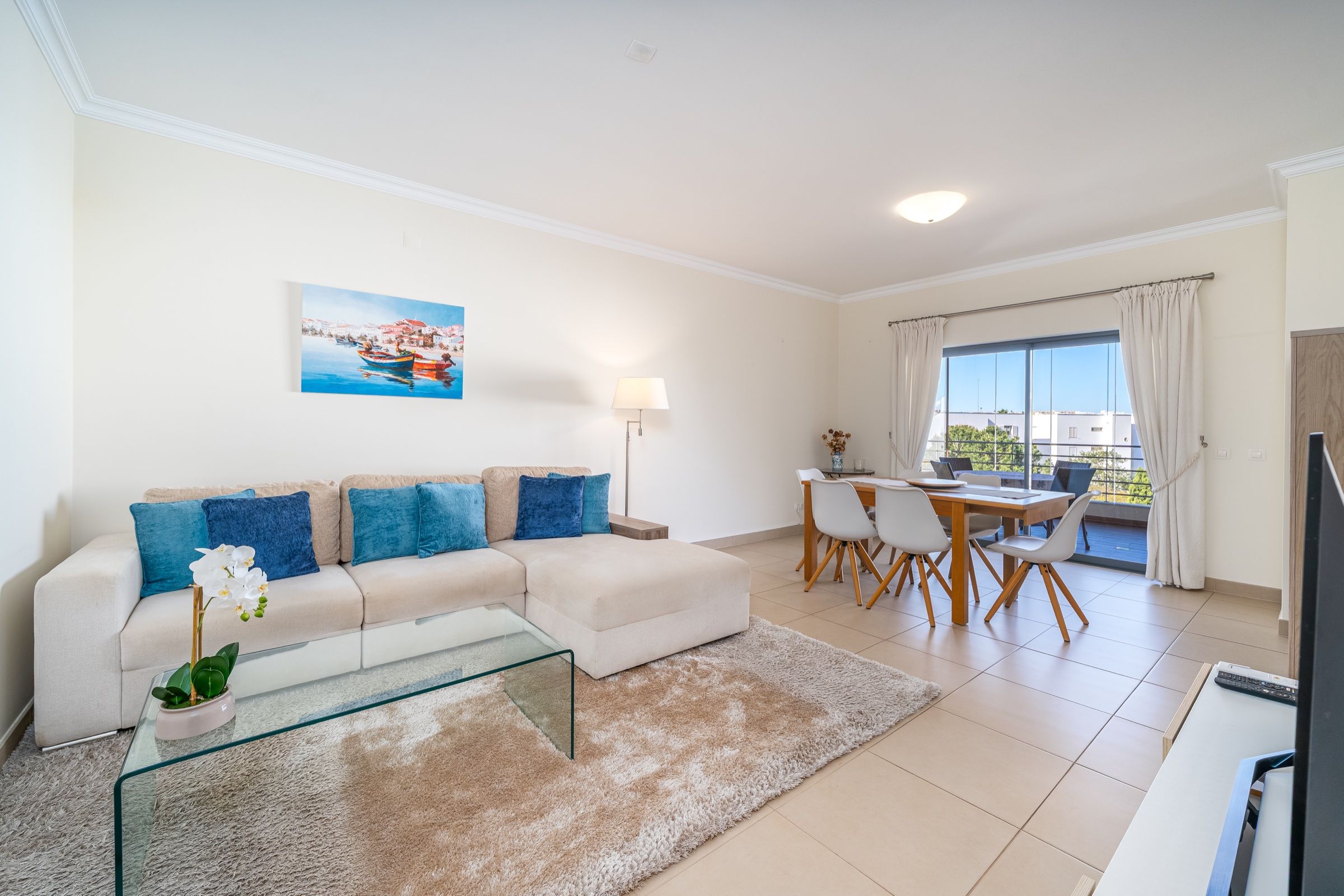 Bright living room with a white corner sofa, blue cushions and a dining table by the window