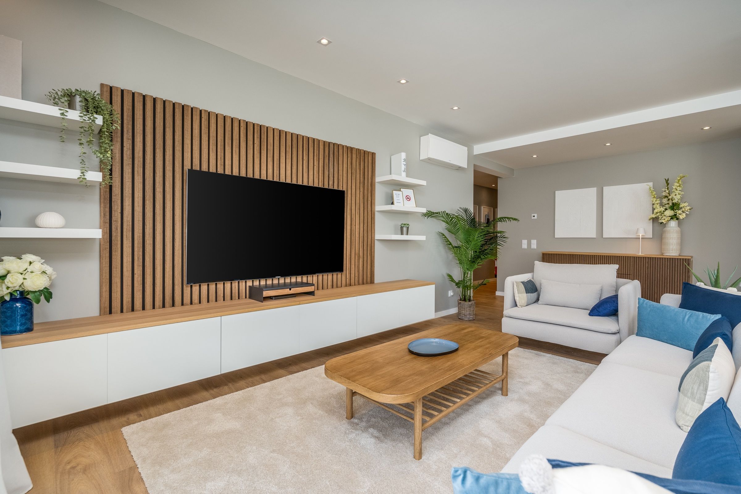 Modern living room with a wooden slat wall, white sofas with blue cushions and a wooden coffee table