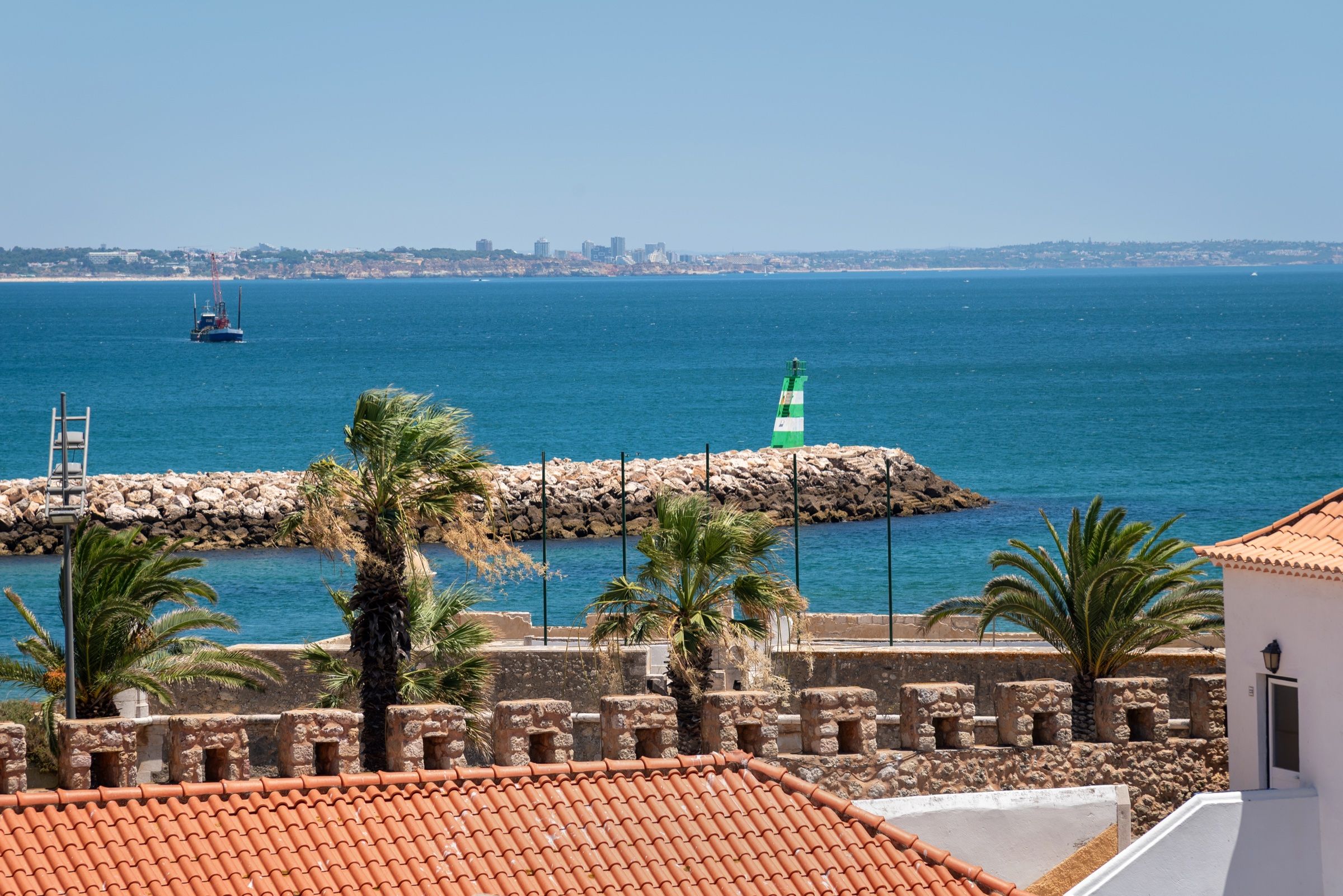 View over rooftops and the town walls to the sea, with the green harbour light and palm trees