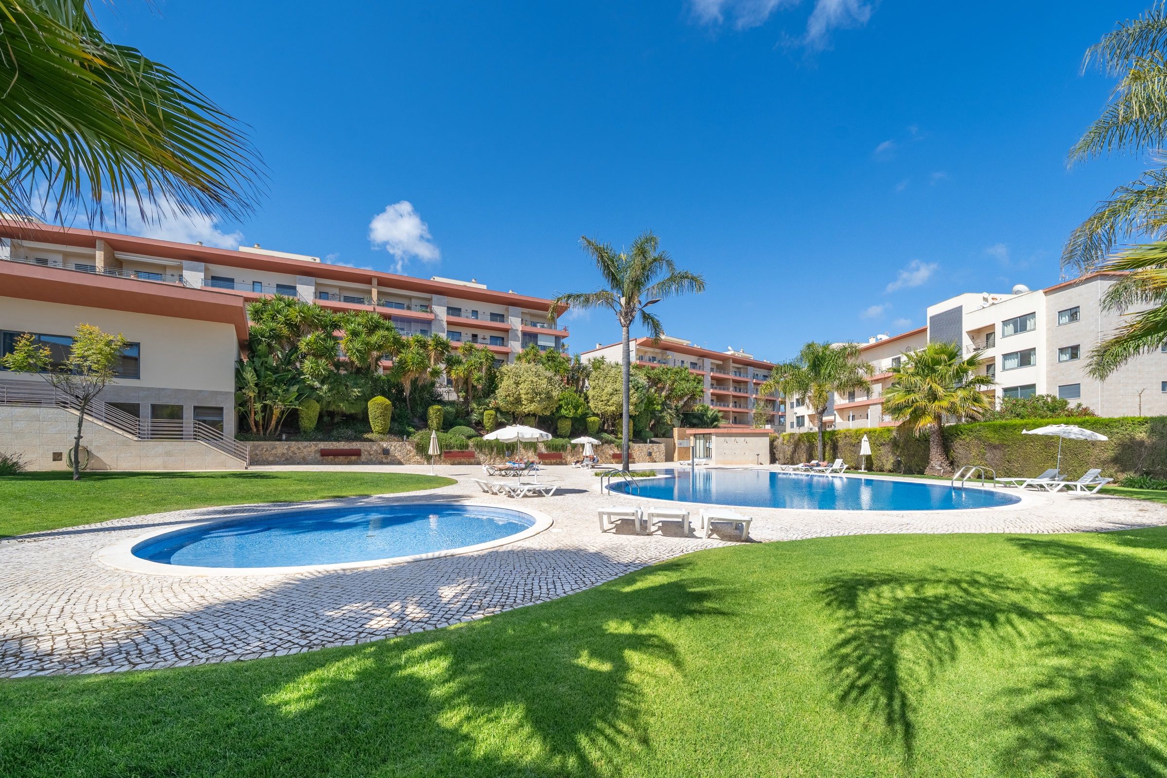 Lawned garden of the apartment complex, with two pools and palm trees