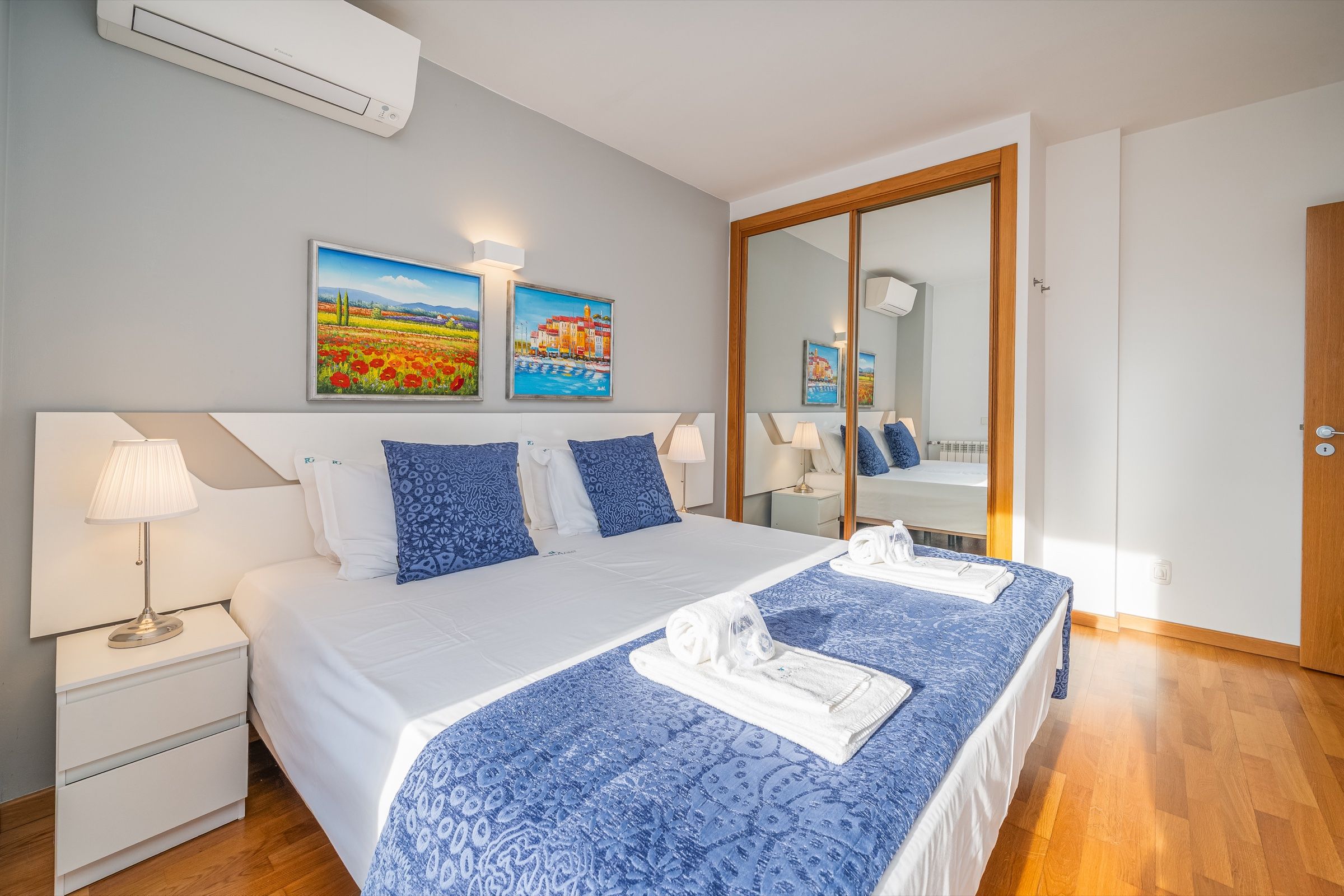 Double bedroom with a blue bedspread, folded towels on the bed and a mirrored wardrobe