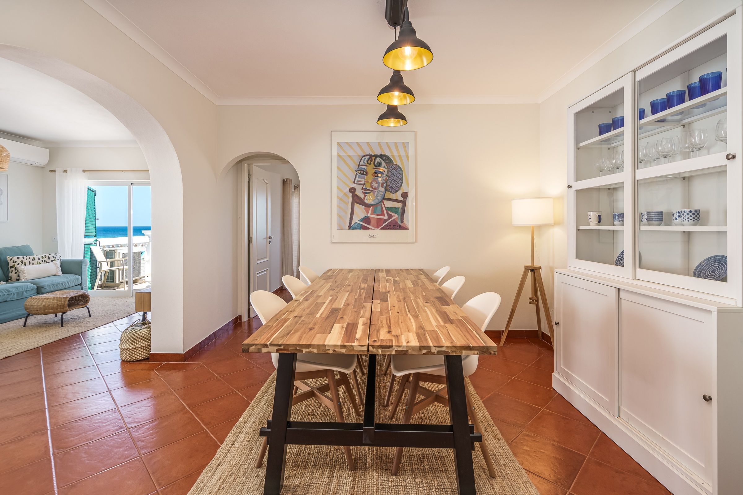 Dining room with a long wooden table, white chairs, arches and a dresser with tableware