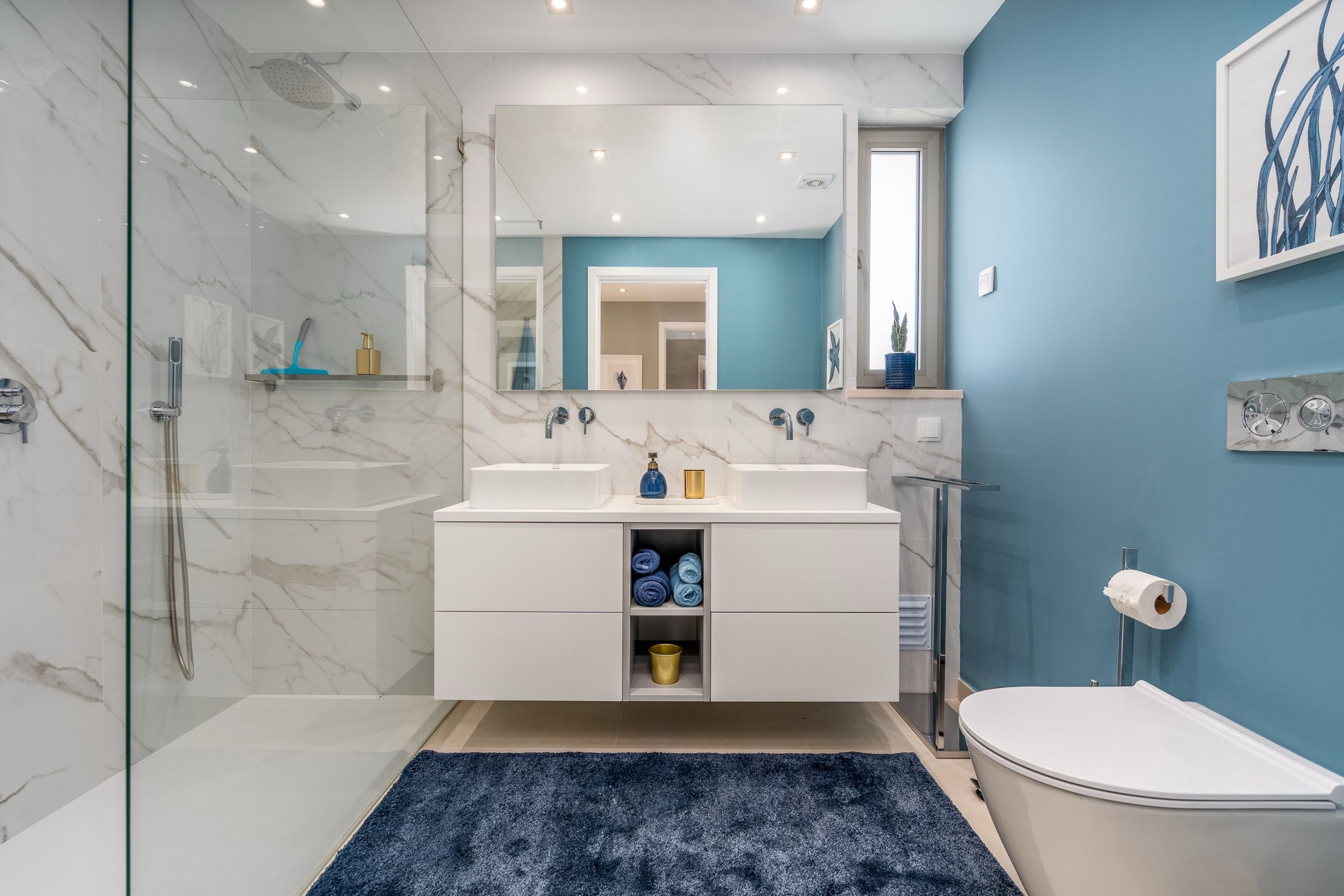Bathroom in white marble with a blue wall, a glass shower and two basins