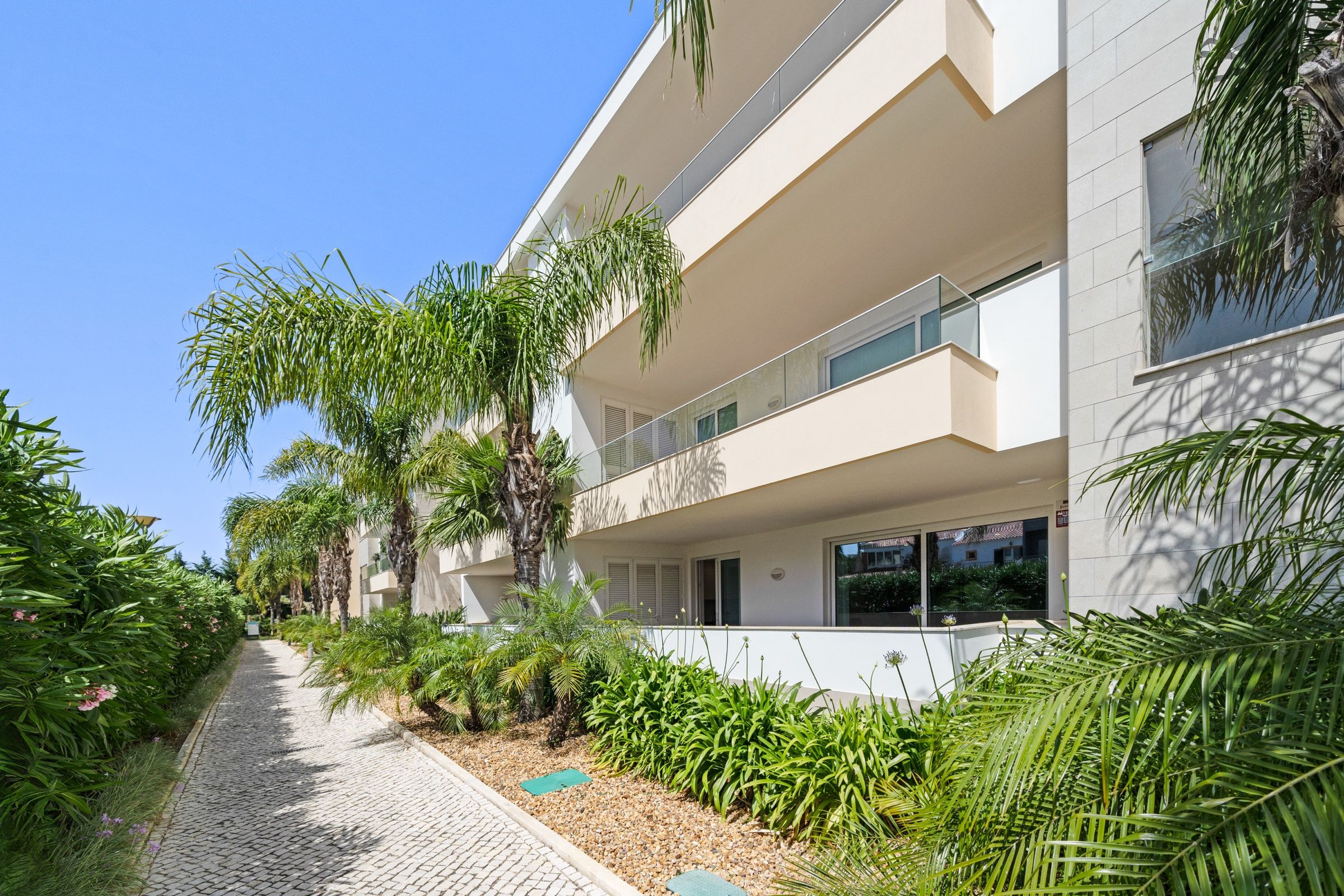 Cobbled path between palm trees and flower beds, beside the apartment building