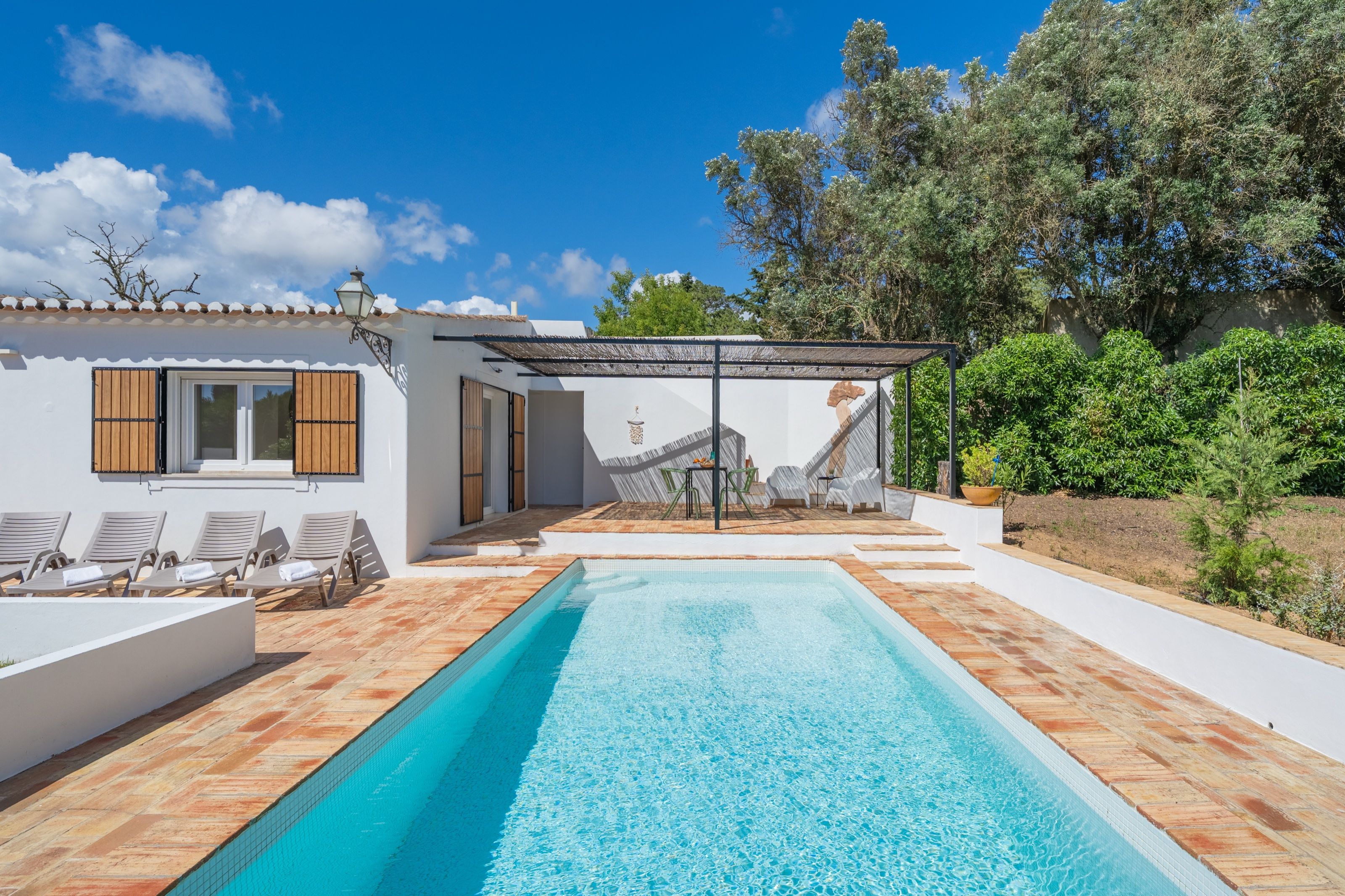 Long pool in front of a white Algarve-style house, with sun loungers and a pergola